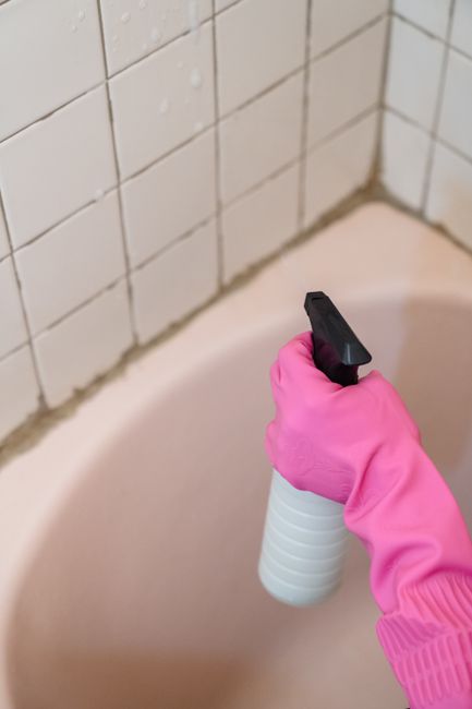 A vacuum cleaner attachment is used to clean a polished wooden floor in a residential setting. The floor has a rich, dark wood grain and is partially illuminated by ambient lighting, highlighting its