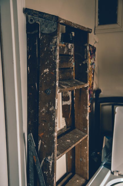 A silver aluminum step ladder with four steps, positioned against a plain, light-colored wall in a room with bright, even lighting. The ladder's surface shows minor signs of wear and is free of clutter or dust, indicating recent or ongoing cleaning activities. The background wall appears clean and smooth, with no visible stains or marks, suggesting a well-maintained environment. The presence of the ladder may imply preparations for cleaning or maintenance work, consistent with surface cleaning and deep cleaning processes by Harringay Carpet Cleaning. No other objects or furniture are visible in the image, highlighting the focus on the ladder and the clean, tidy space.